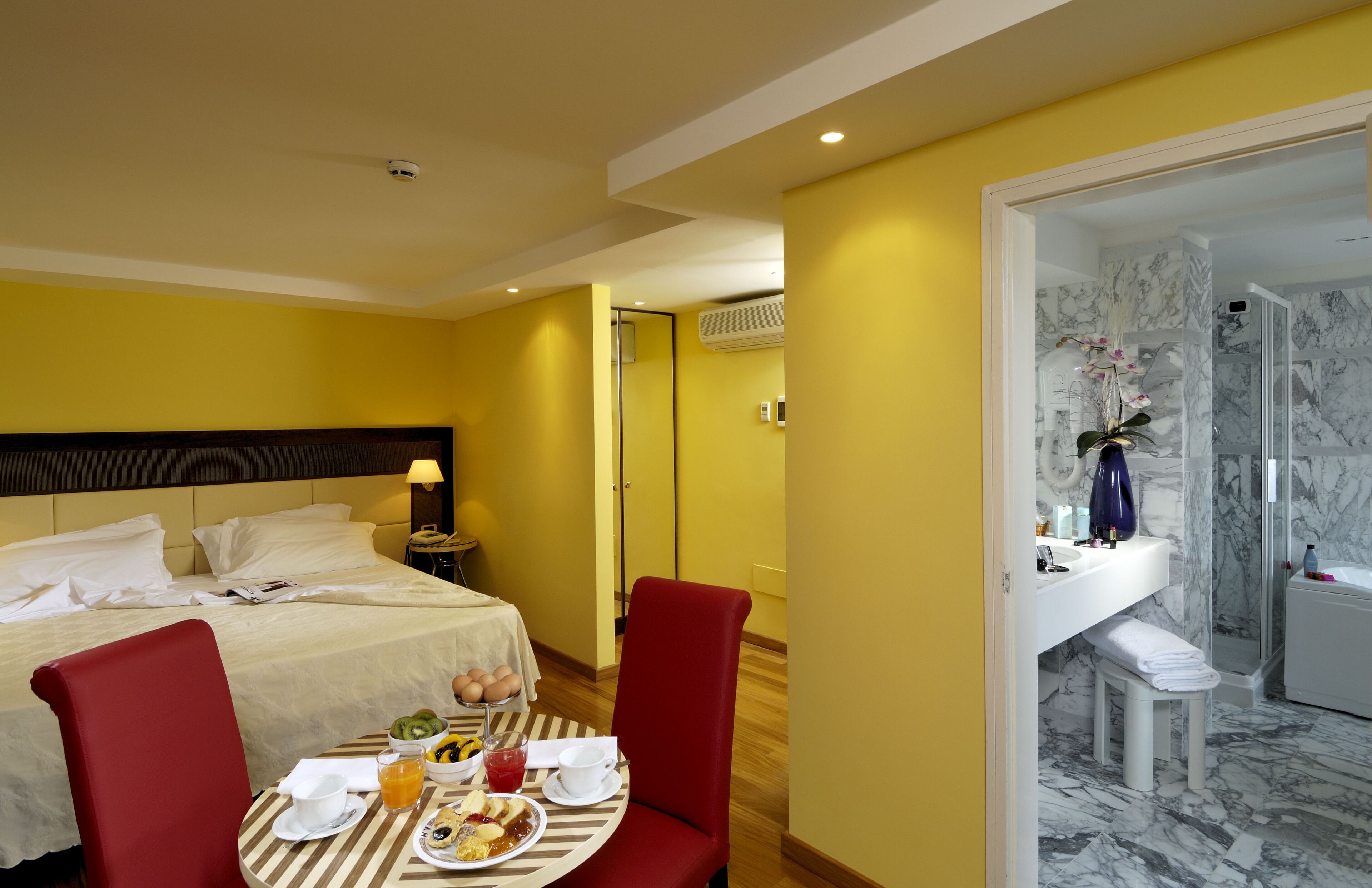 Ein Hotelzimmer mit Bett, Frühstückstisch und einem Badezimmer mit Dusche und Marmorwänden.