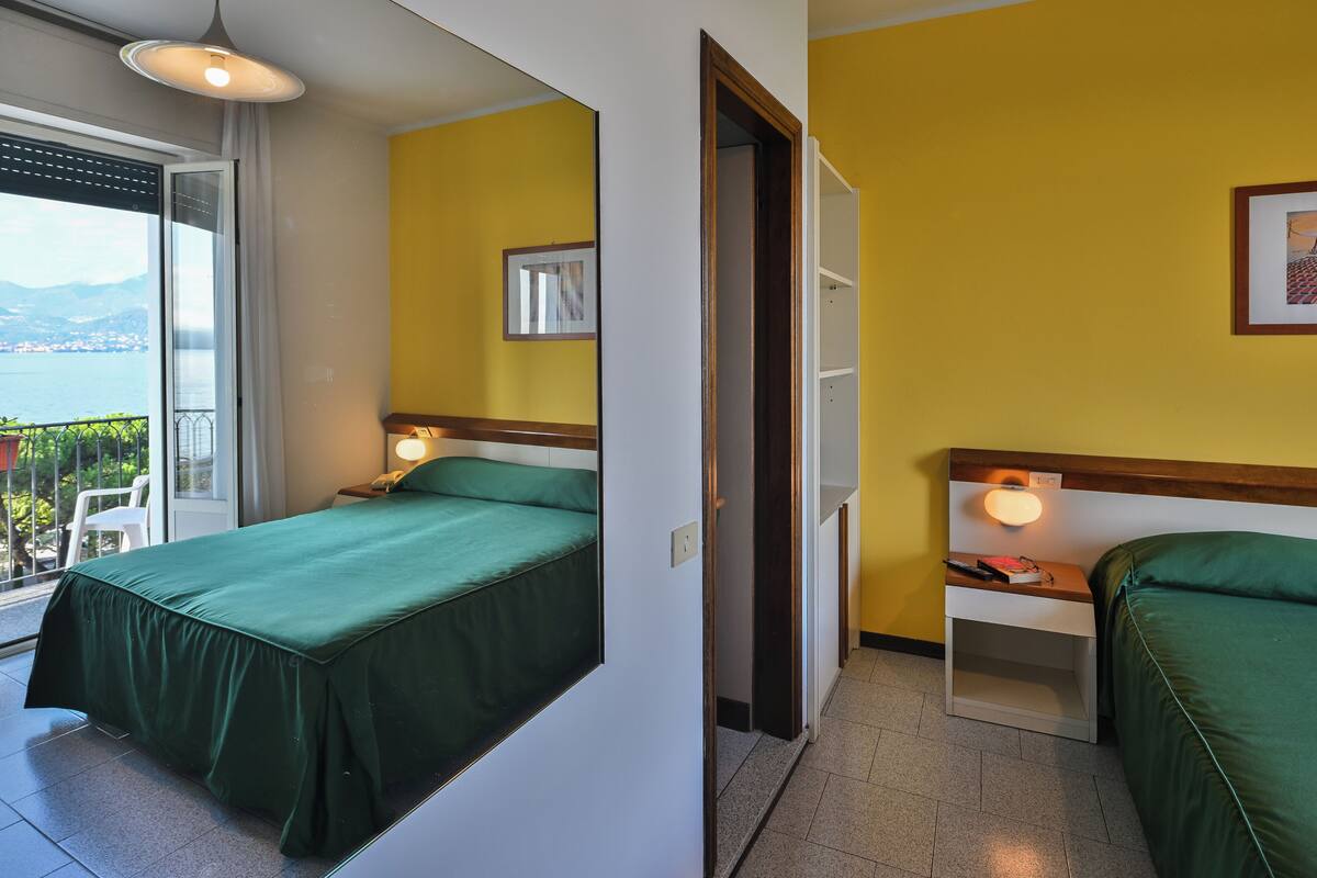 Une chambre d’hôtel avec deux lits, un balcon donnant sur la mer et une petite table avec une lampe.