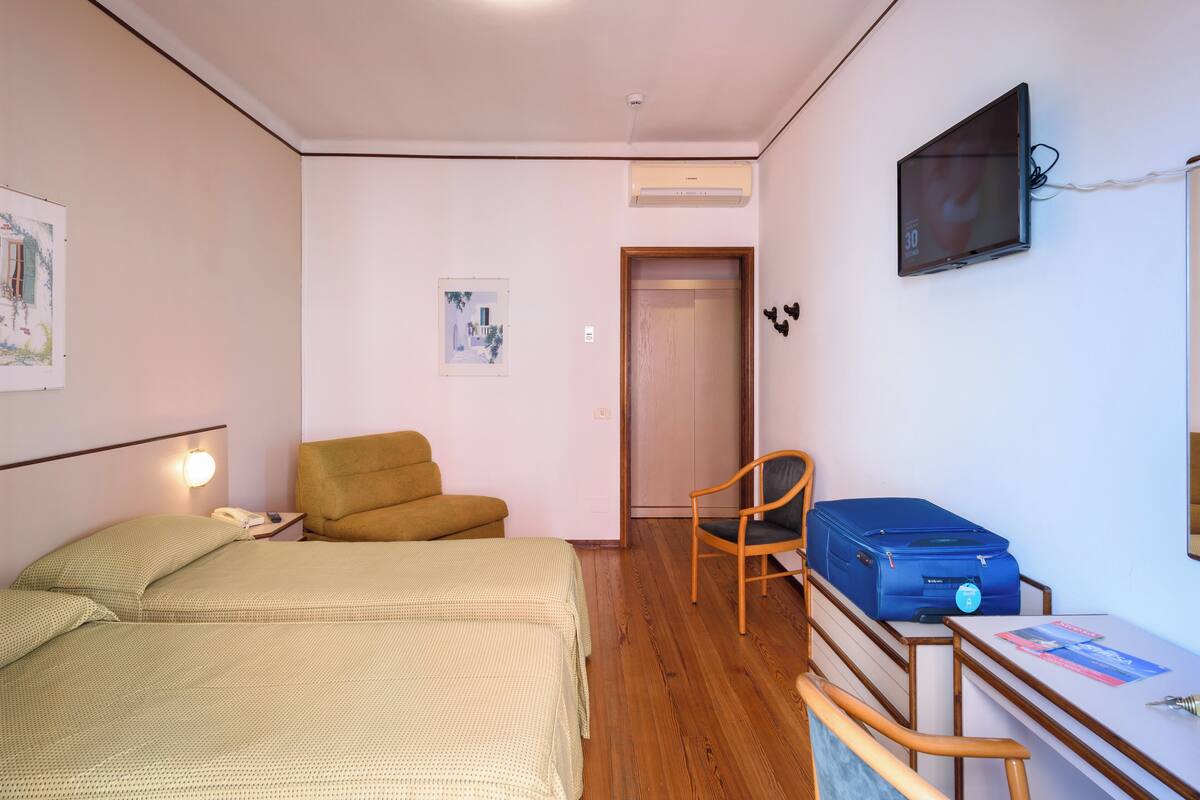 Une chambre à coucher avec un lit, une chaise, un bureau, une valise et un téléviseur fixé au mur.