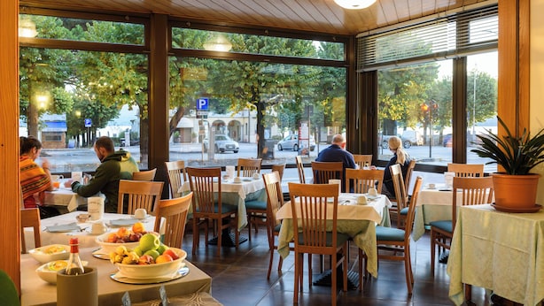 A restaurant with wooden tables and chairs, large windows with a view of the street, and a variety of dishes on the tables. - Hotel Italie Et Suisse (Stresa)