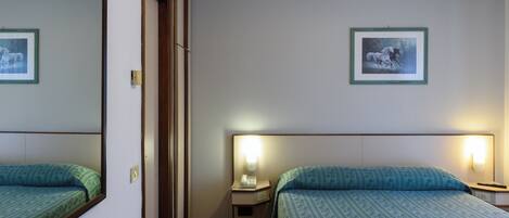 A hotel room with two beds, a nightstand with a lamp, and two framed pictures on the wall.