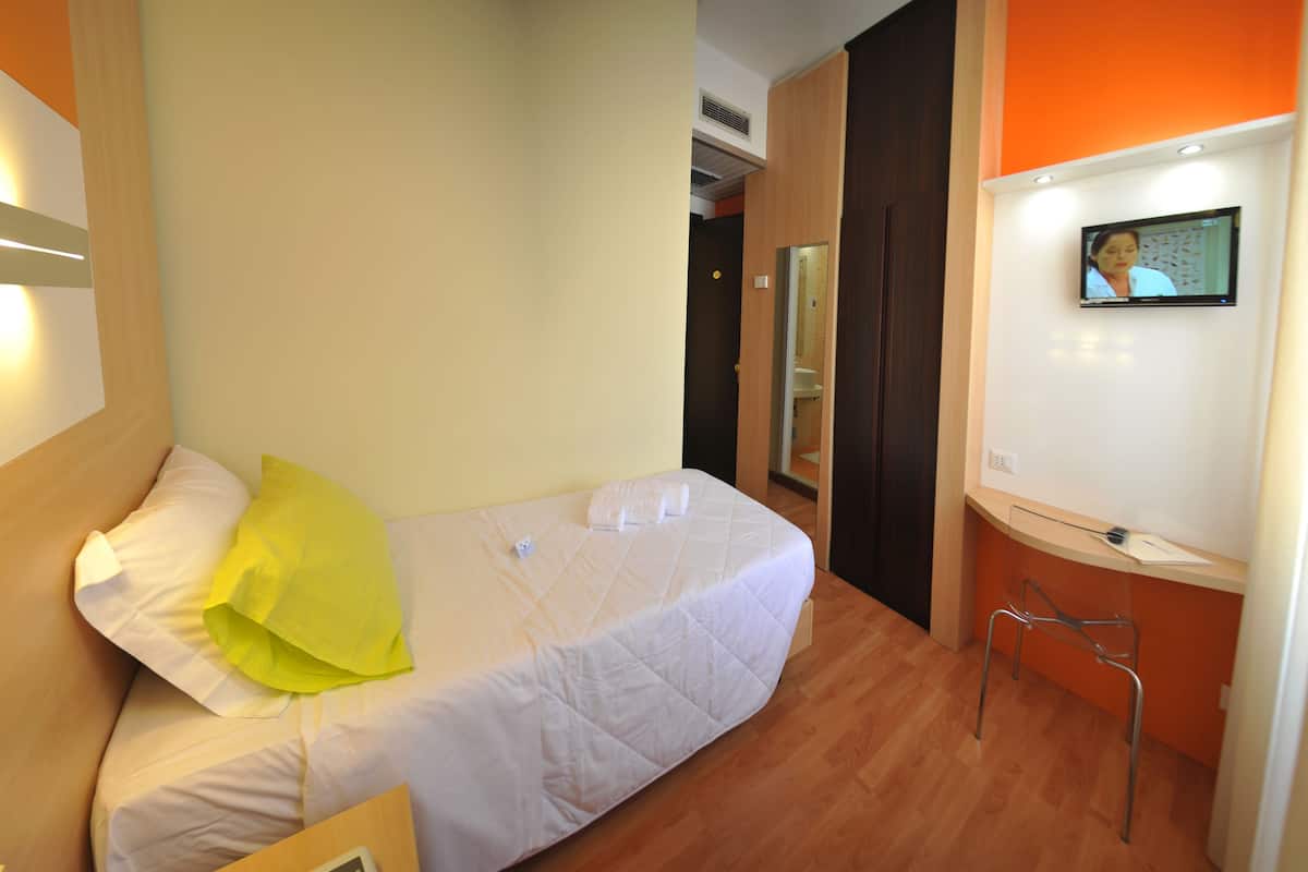 A hotel room with a bed, a TV on the wall, and a wooden floor.