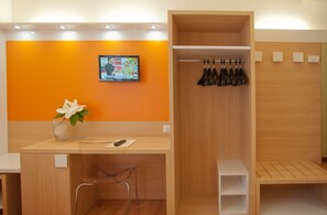 Zona de recepción de hotel con un mostrador de madera, un televisor en la pared y un zapatero.