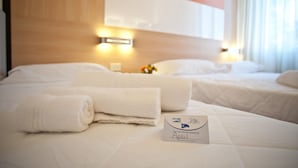 A hotel room with two beds, white linens, a headboard with integrated lighting, and a sign indicating room service availability. - Hotel Rodia (Maglie)