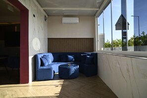 A modern living room with a blue sectional sofa, a round ottoman, and a wooden slatted wall. - Puteoli Palace Hotel (Pozzuoli)
