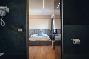 Une chambre d’hôtel moderne avec un grand lit, une table de chevet, un miroir et un sèche-cheveux fixé au mur.