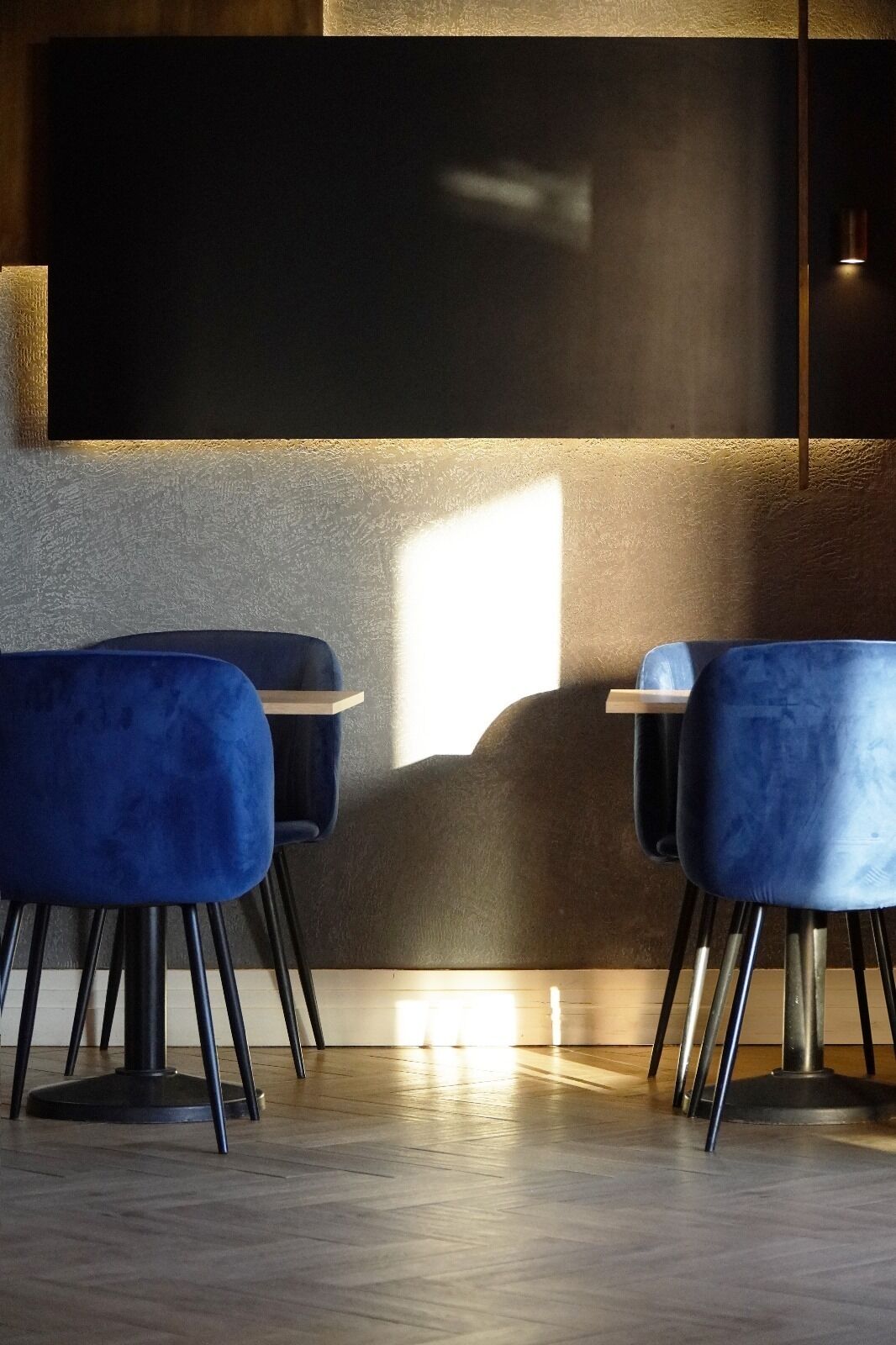 A modern interior with two blue upholstered chairs, a wooden table, and a large blackboard on the wall.