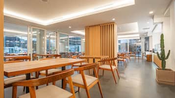 Un comedor moderno con mesas y sillas de madera, ventanas amplias y una planta de cactus.