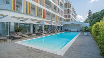 Un hôtel moderne doté d’une piscine, de chaises longues et d’un espace salon abrité.