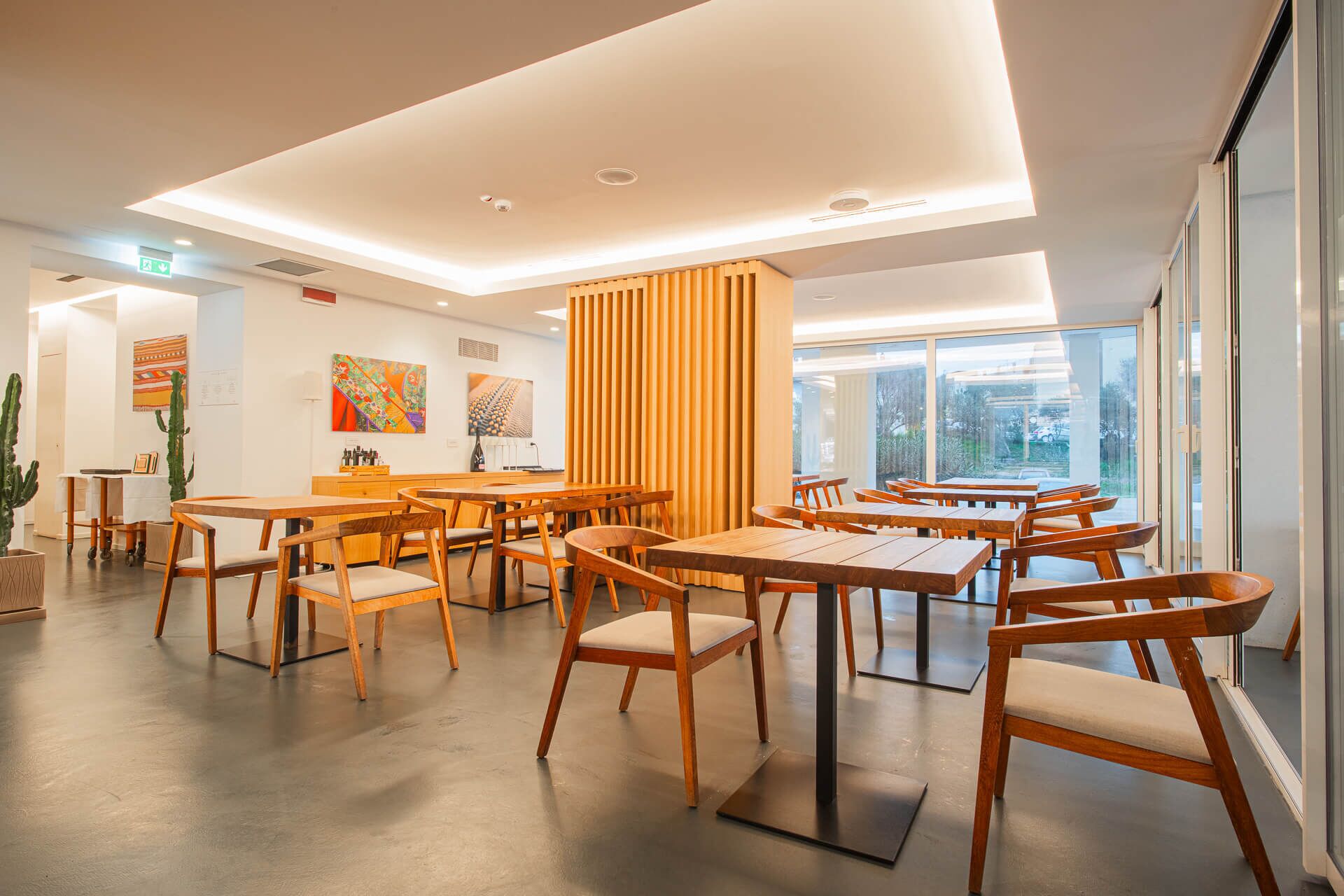 A modern dining area with wooden tables and chairs, a central column, and artwork on the walls.
