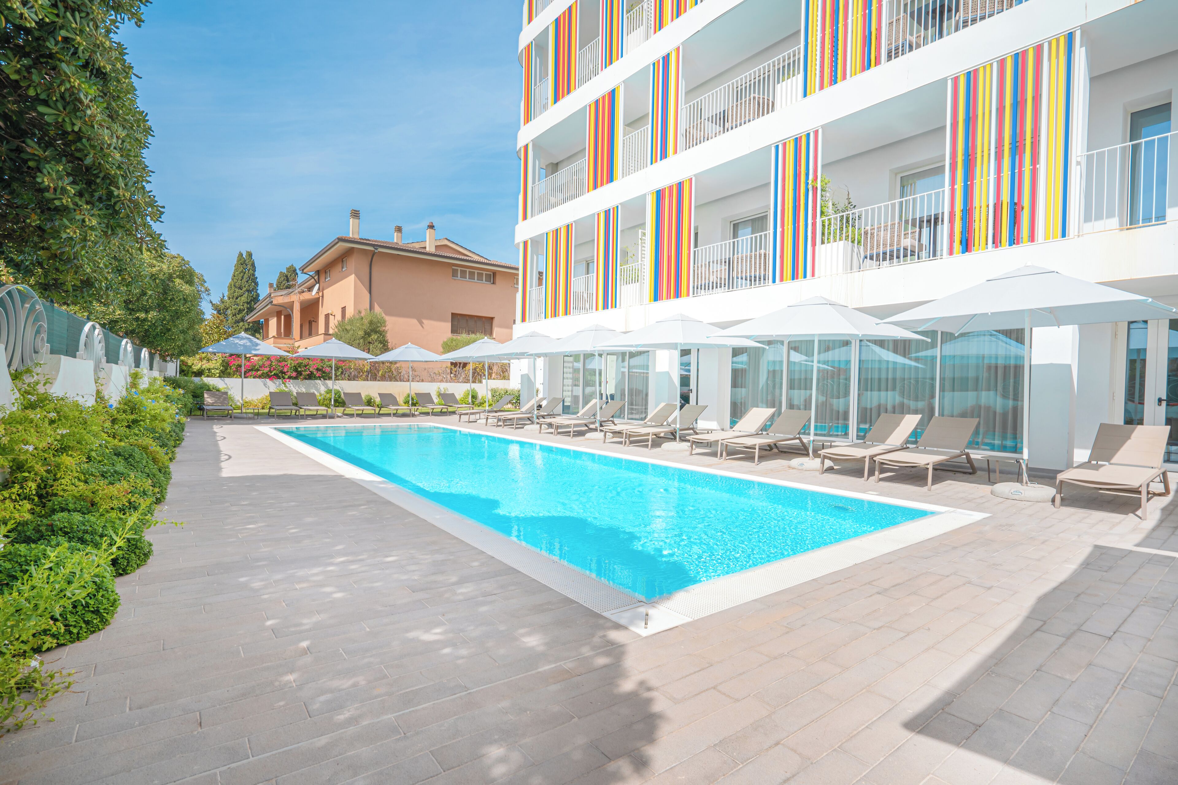 A swimming pool with lounge chairs and umbrellas, surrounded by a multi-story building with balconies.