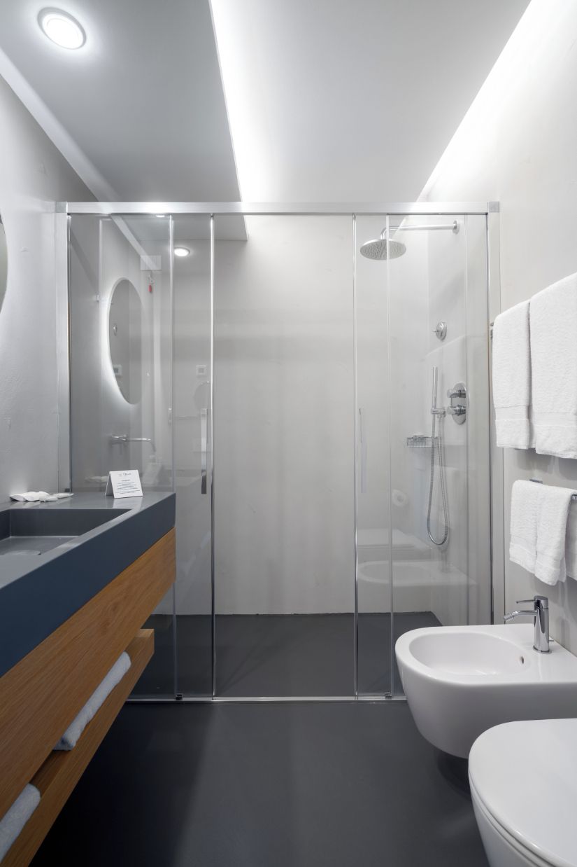 Un baño moderno con cabina de ducha de vidrio, tocador de madera, lavamanos blanco y un bidé.