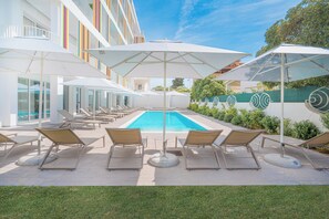 A poolside area with sun loungers and umbrellas, a clear blue pool, and a modern building with balconies.