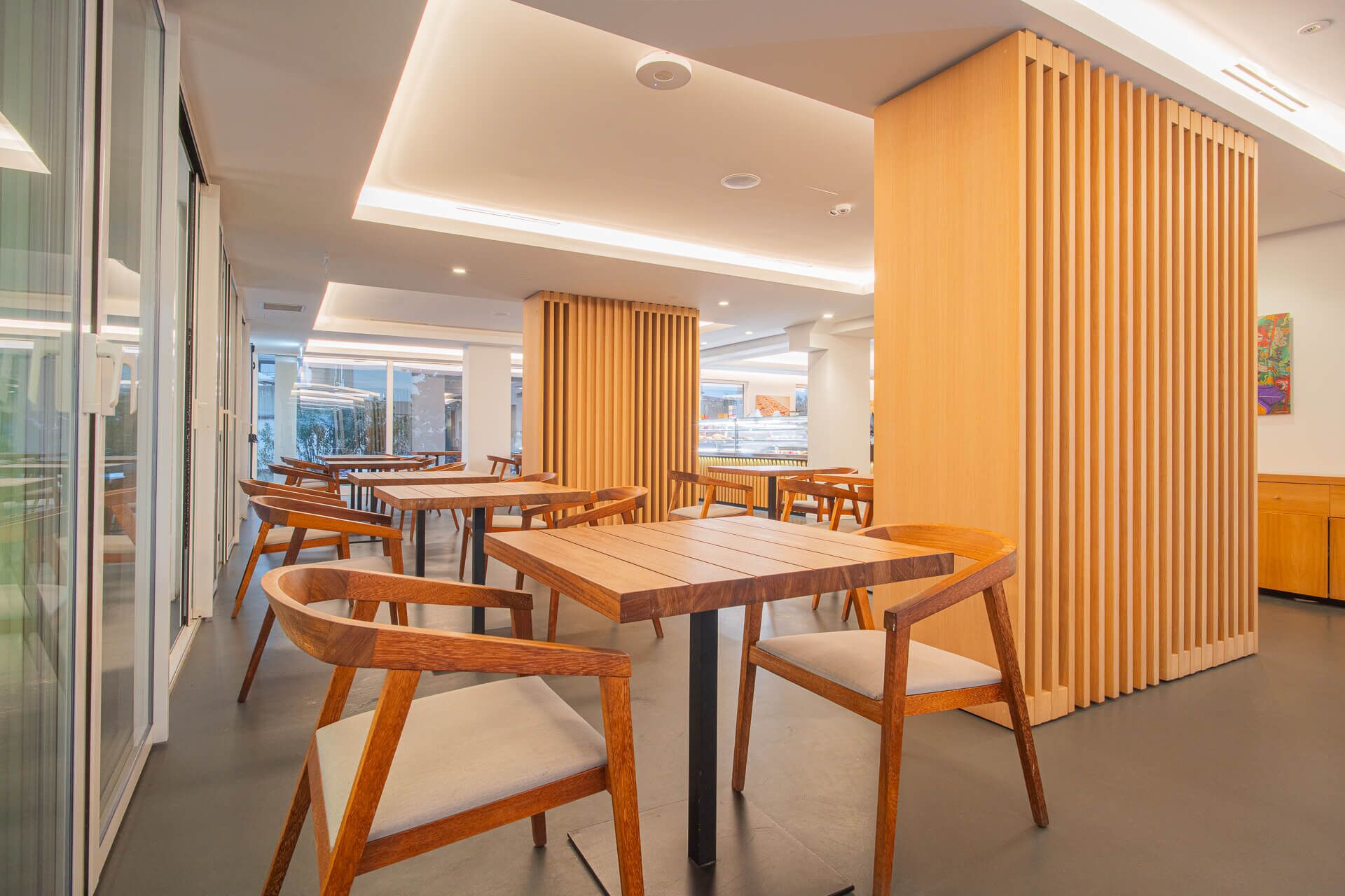 Un interior de restaurante moderno con mesas y sillas de madera, una pared de vidrio y vistas a la ciudad.