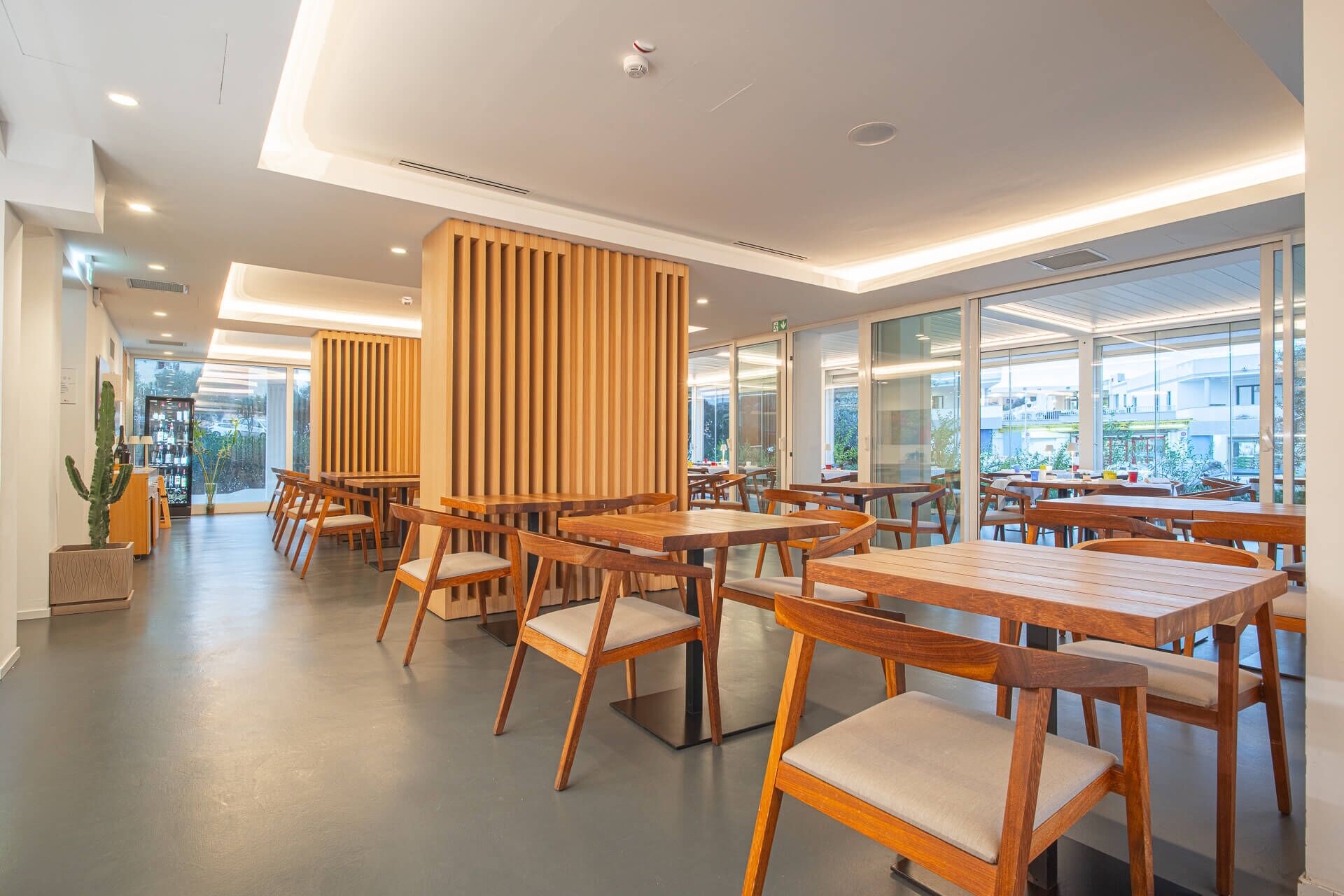 Ein modernes Restaurant mit Holztischen und -stühlen, großen Fenstern und Blick ins Freie.