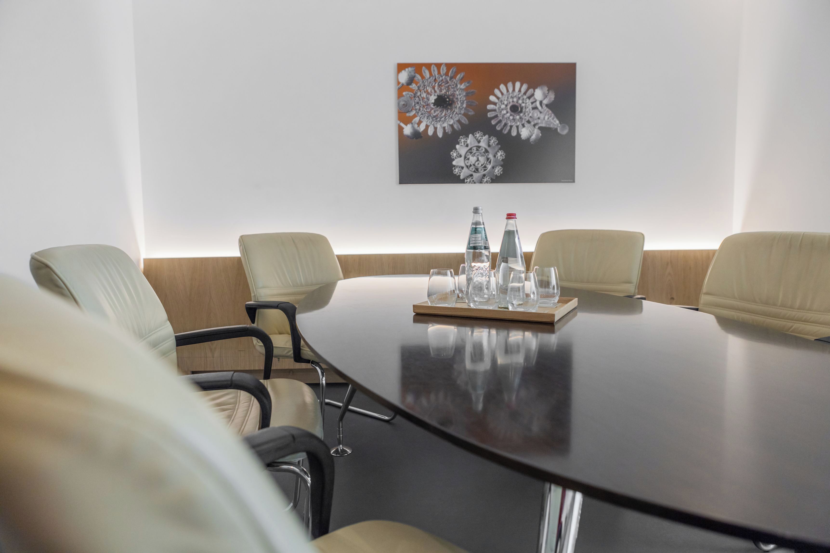 A conference room with a long table, four chairs, and a wall-mounted painting.