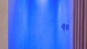 A room with a blue-lit ceiling, a visible light switch, and a wooden panel on the right wall.