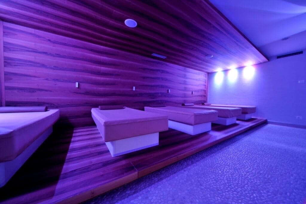 A room with wooden panel walls and a carpeted floor. There are several rectangular seating areas with cushions.