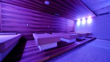 A room with wooden panel walls and a carpeted floor. There are several rectangular seating areas with cushions.
