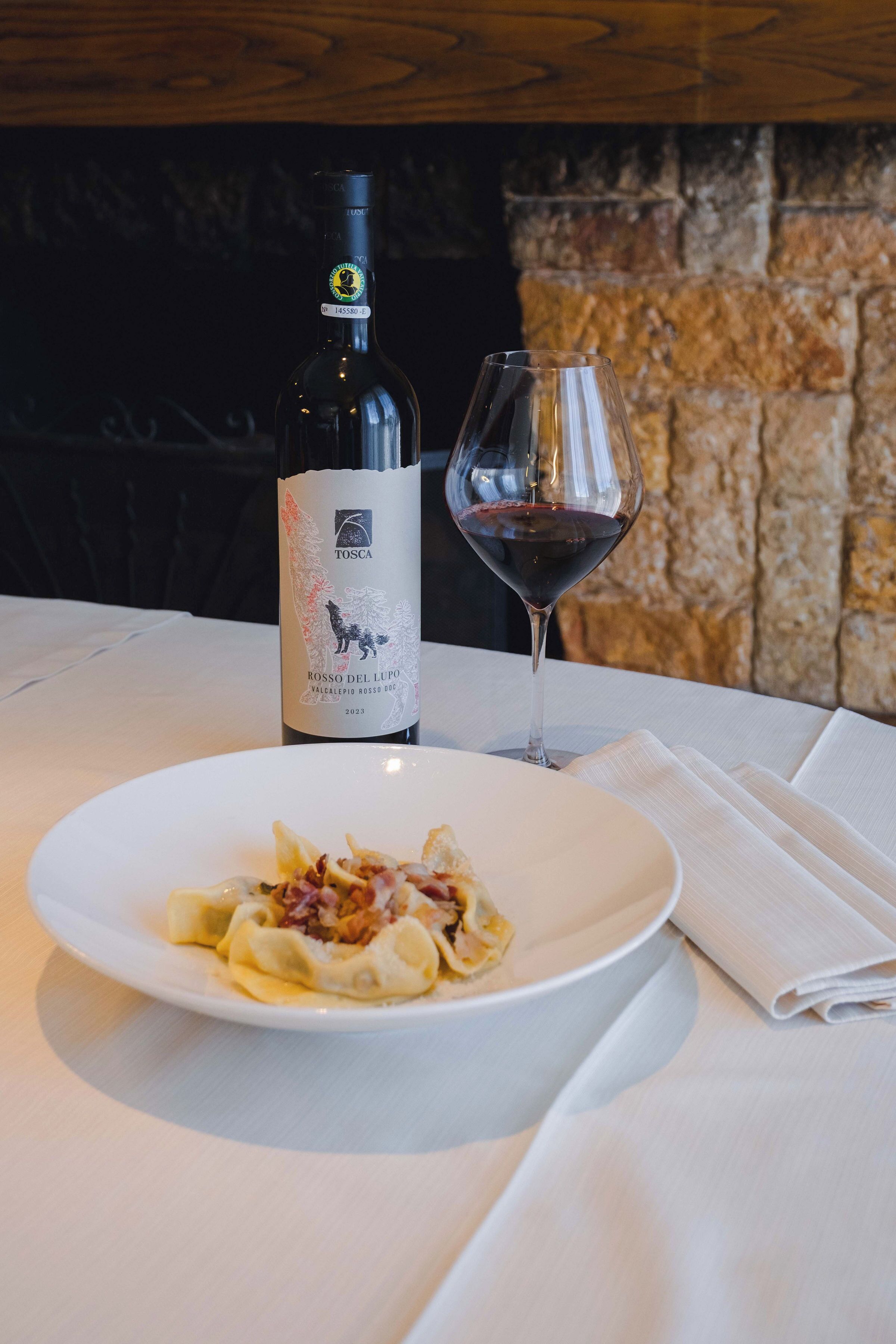 A bottle of wine and a glass on a table with a plate of food.