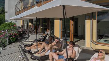 Área à beira da piscina com espreguiçadeiras, guarda-sóis e um edifício com varandas.