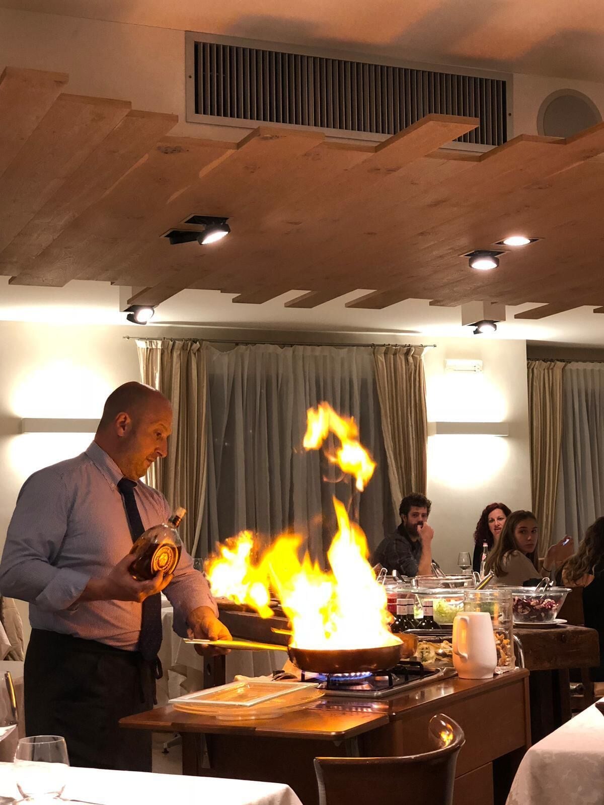 Interior de restaurante mostrando un chef preparando un flambé, una mesa de comensales y un diseño moderno en el techo.