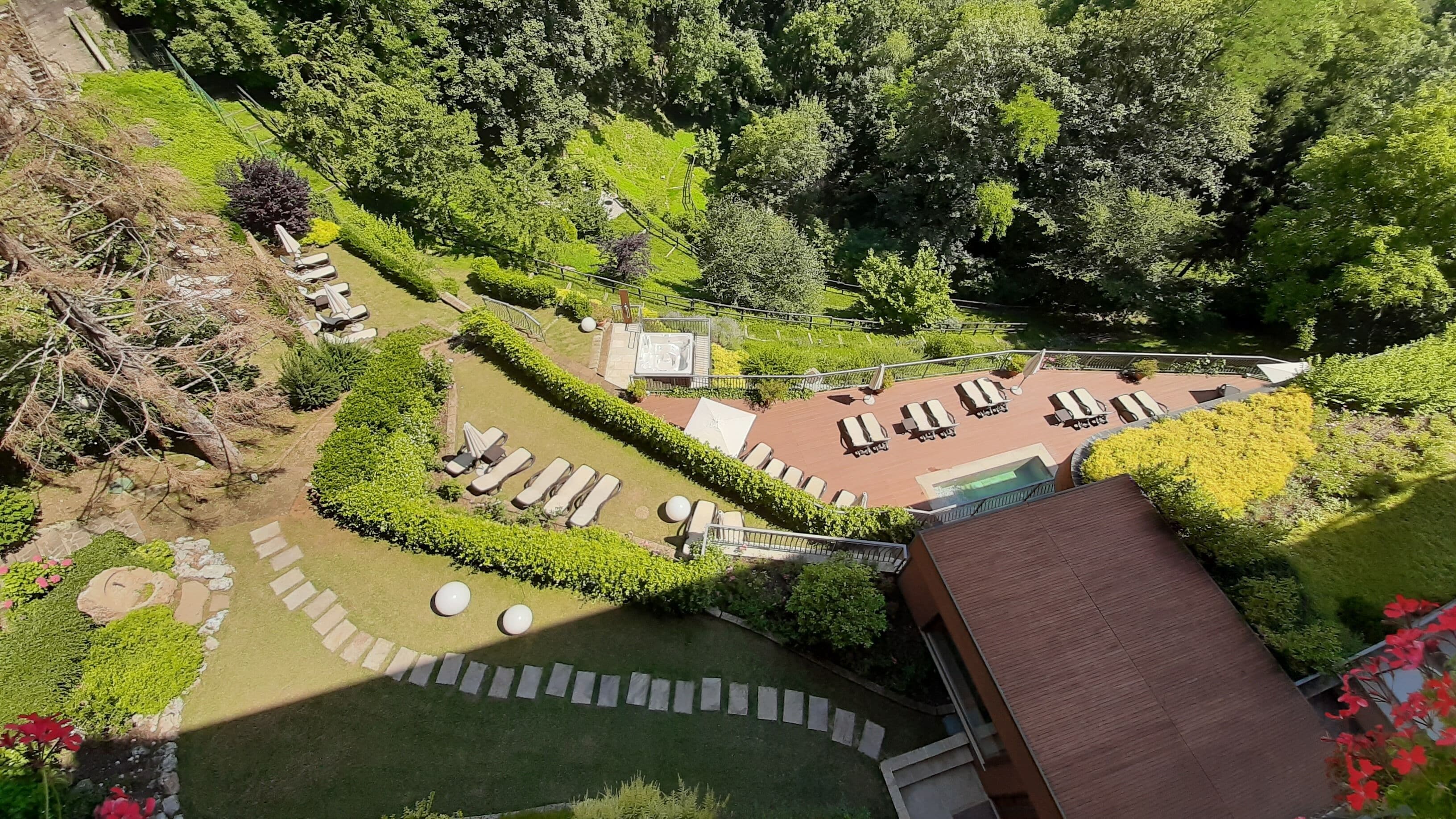 Vista aérea de un complejo turístico con zona de piscina, tumbonas y un jardín cuidado.
