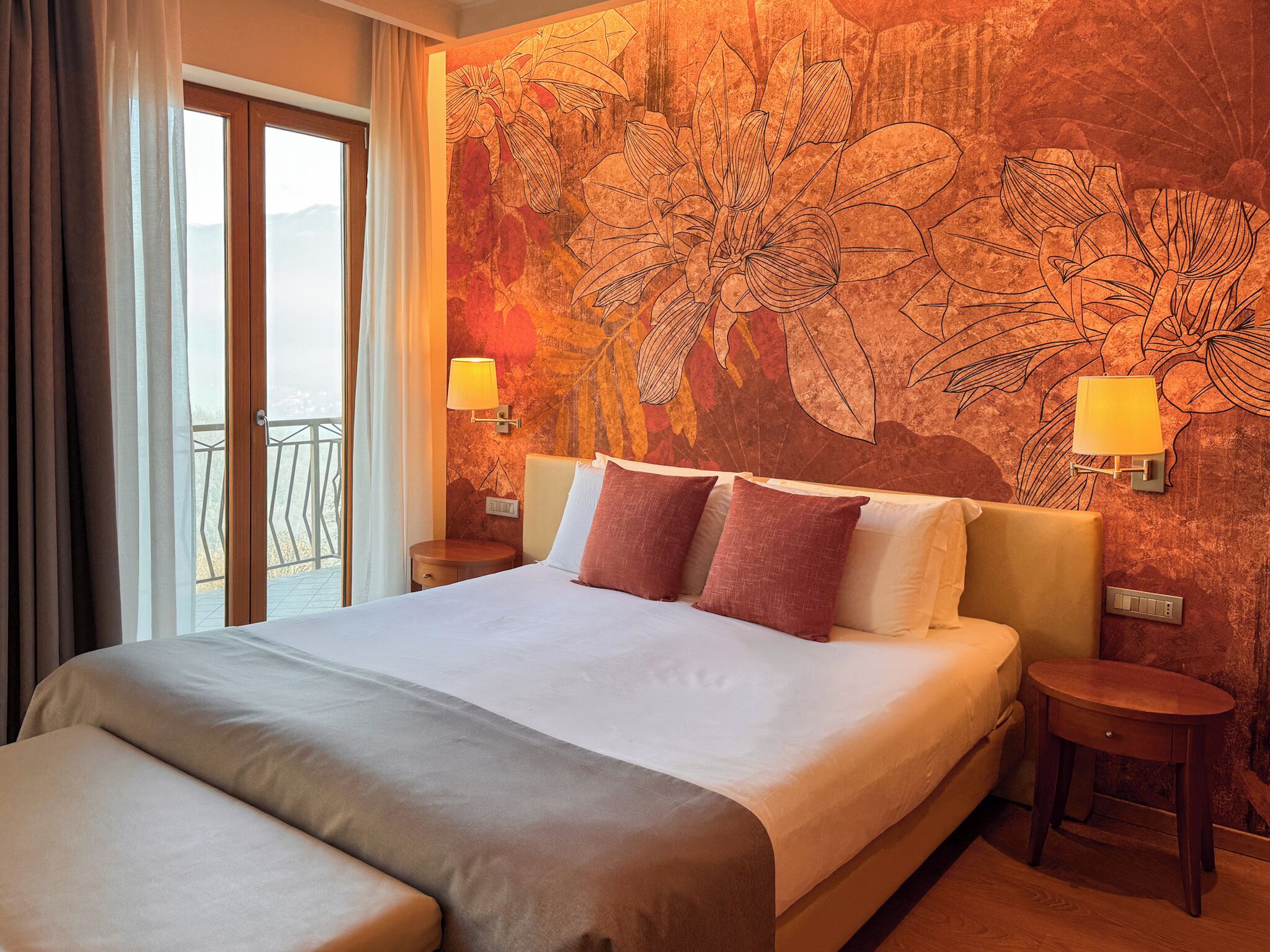 Une chambre d’hôtel avec un grand lit, deux lampes de chevet, une table de chevet, un plancher en bois et une vue sur l’extérieur.