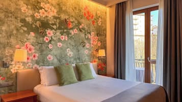 Ein Hotelzimmer mit einem großen Bett, zwei Nachttischen, einer Wand mit floralem Wandpapier und einem Fenster mit Vorhängen.