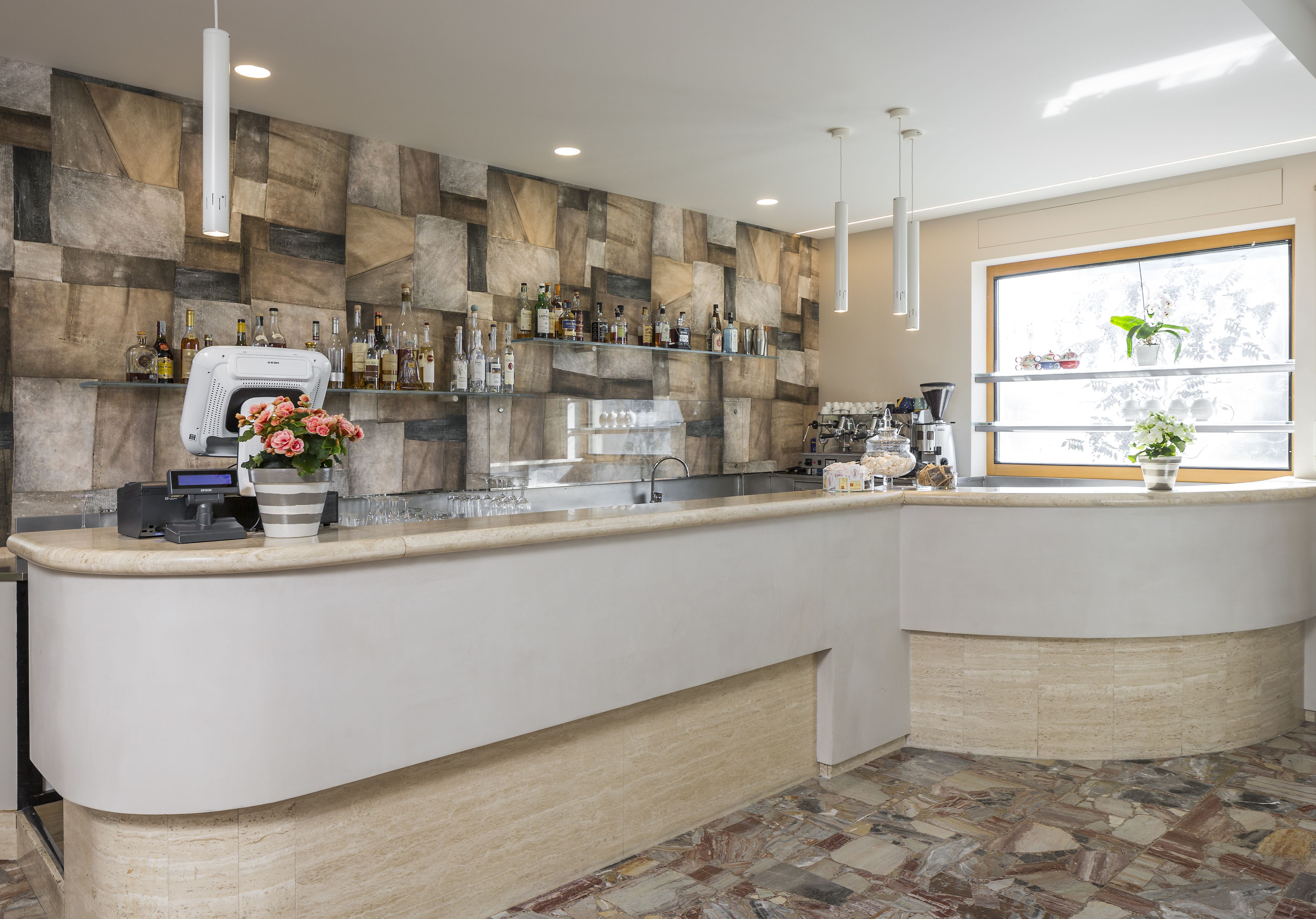 A modern bar area with a stone wall backdrop, a cash register, and a window with a view of trees.