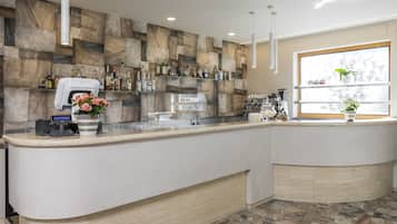 A modern bar area with a stone wall backdrop, a cash register, and a window with a view of trees.