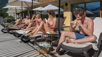 Un área junto a la piscina con sillones de descanso, sombrillas y una cesta de mimbre.