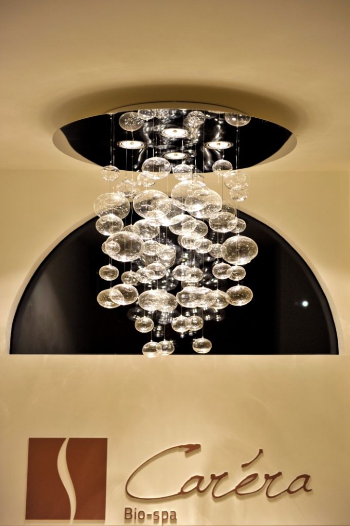A chandelier with multiple clear glass orbs hanging from a black ceiling. Below the chandelier, there is a sign with the text "Carreira Bio-spa".