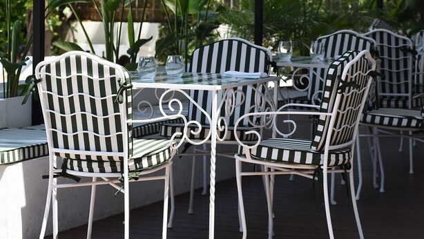 A covered outdoor seating area with metal chairs and tables, surrounded by greenery and a view of trees and plants. - Grand Hotel Flora (Sorrento)