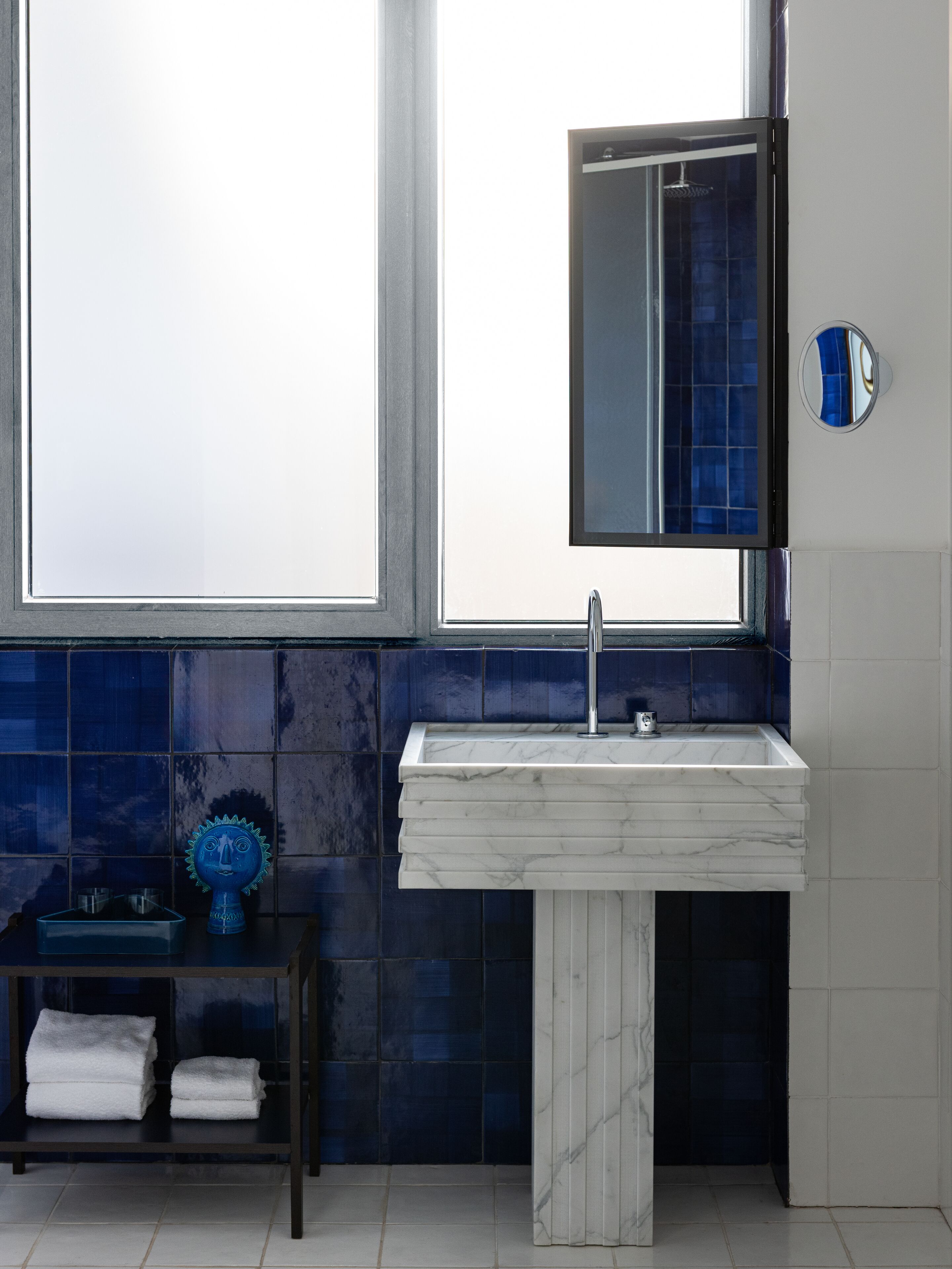 Casa de banho com lavatório de mármore branco, espelho e parede revestida com azulejos azuis.