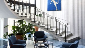 A modern lobby with a staircase, a chandelier, a blue artwork, and seating area. - Grand Hotel Flora (Sorrento)