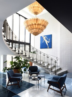 A modern lobby with a staircase, a chandelier, a blue artwork, and seating area. - Grand Hotel Flora (Sorrento)