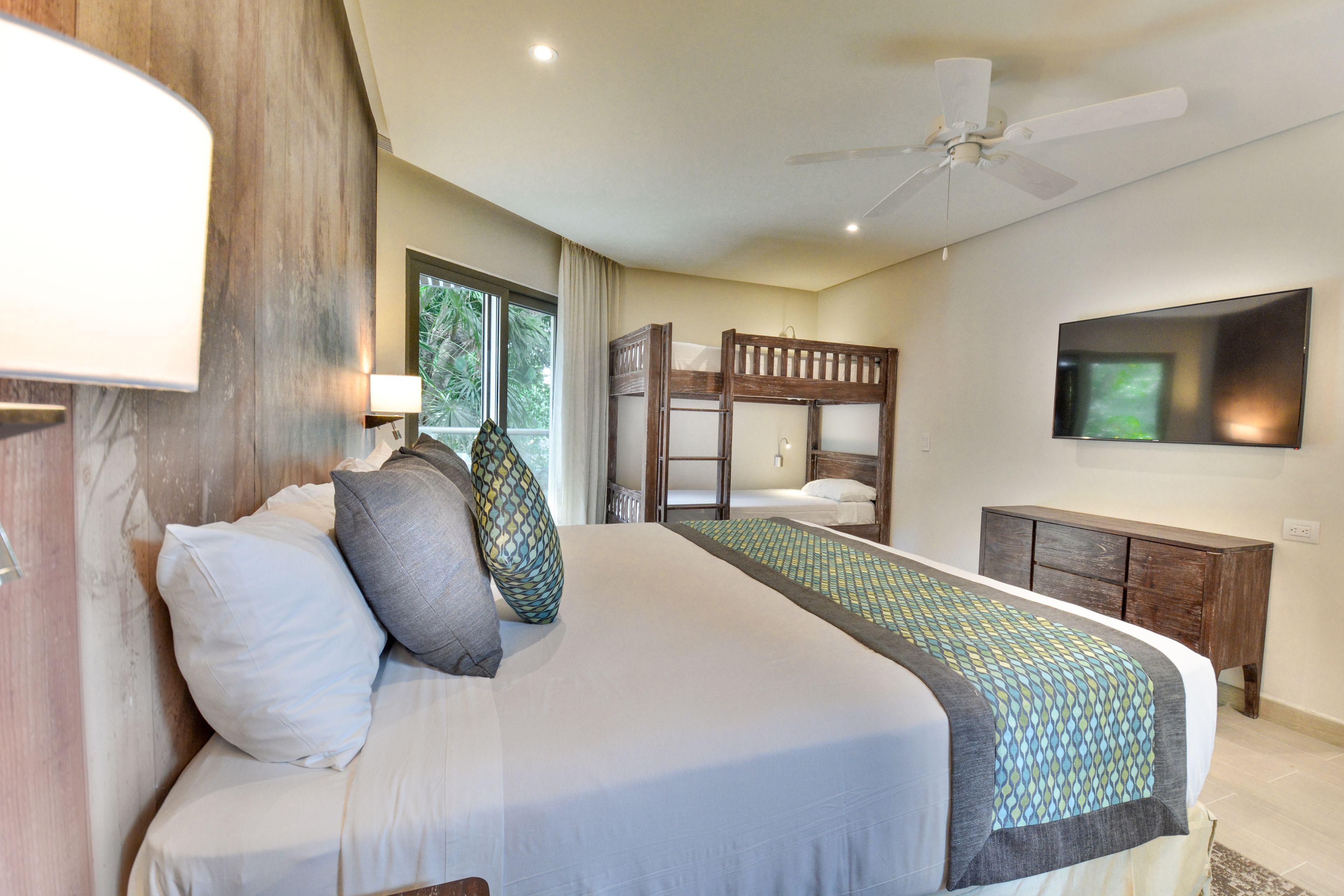 A bedroom with a bunk bed, a flat-screen TV, a ceiling fan, and a window with curtains.