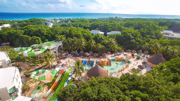 Un complexe hôtelier doté d’un parc aquatique comprenant des toboggans et des piscines, entouré d’une végétation luxuriante et offrant une vue sur l’océan.
