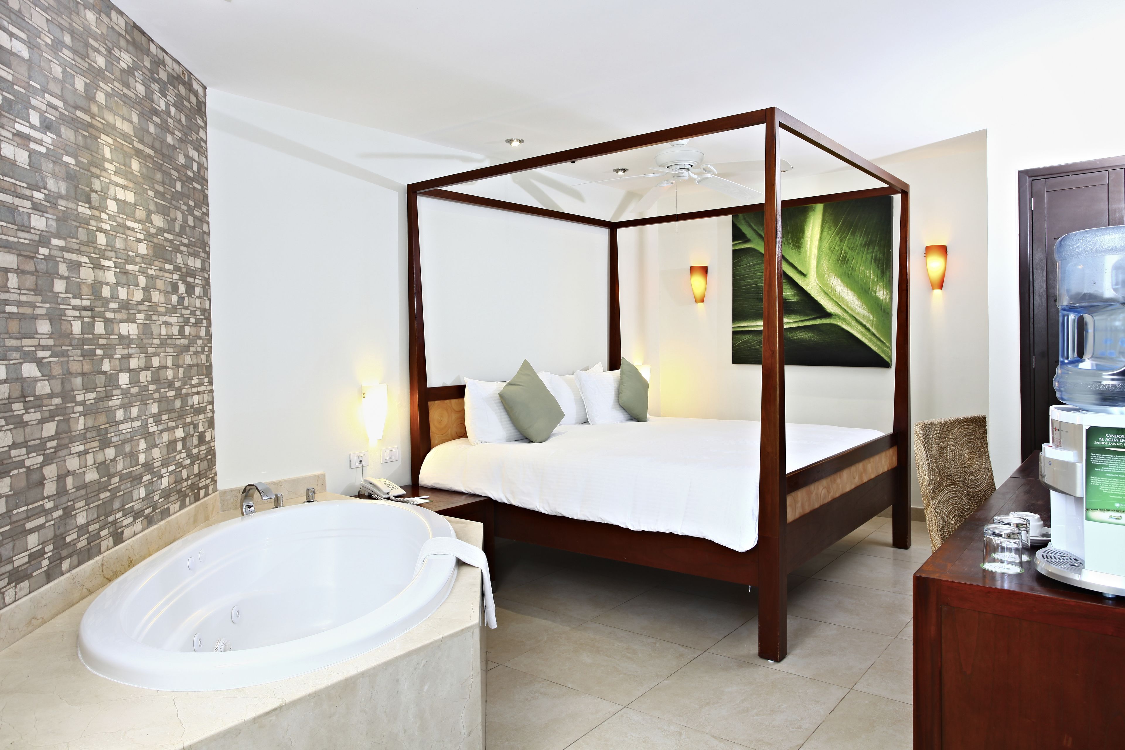 Una cama con dosel y estructura de madera, una bañera grande y un dispensador de agua instalado en la pared.