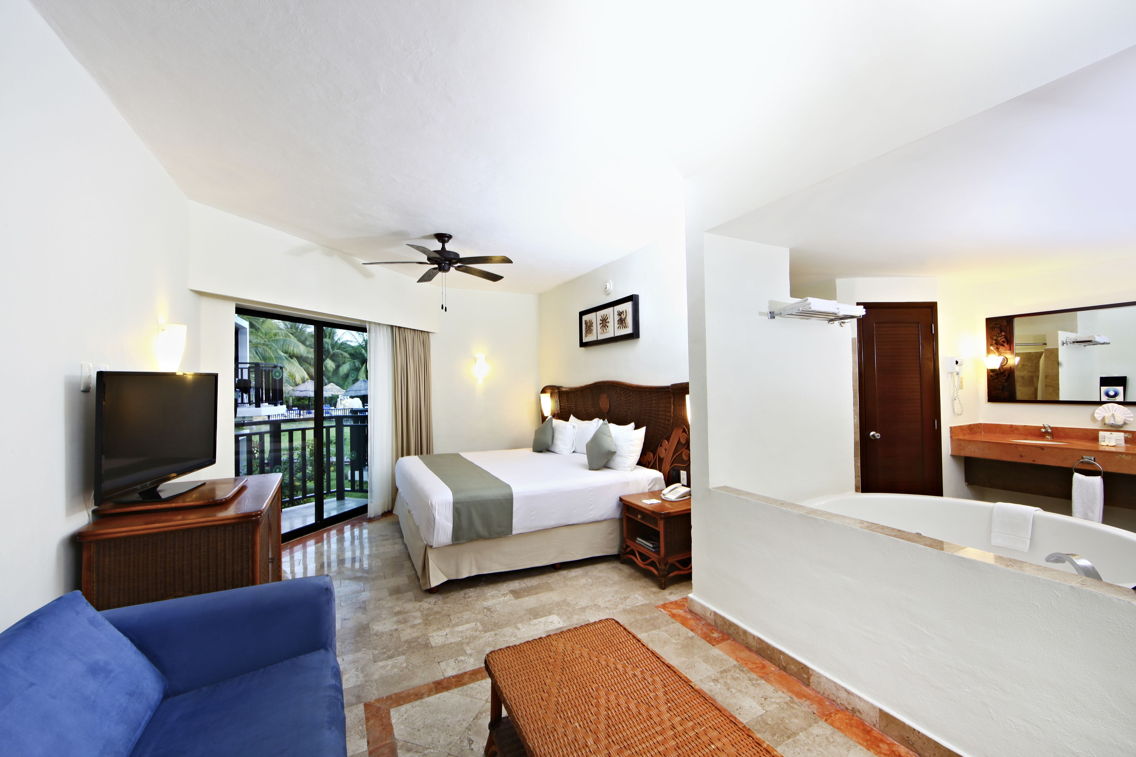 A hotel room with a bed, a TV, a sofa, a bathroom with a bathtub, and a balcony with a view.