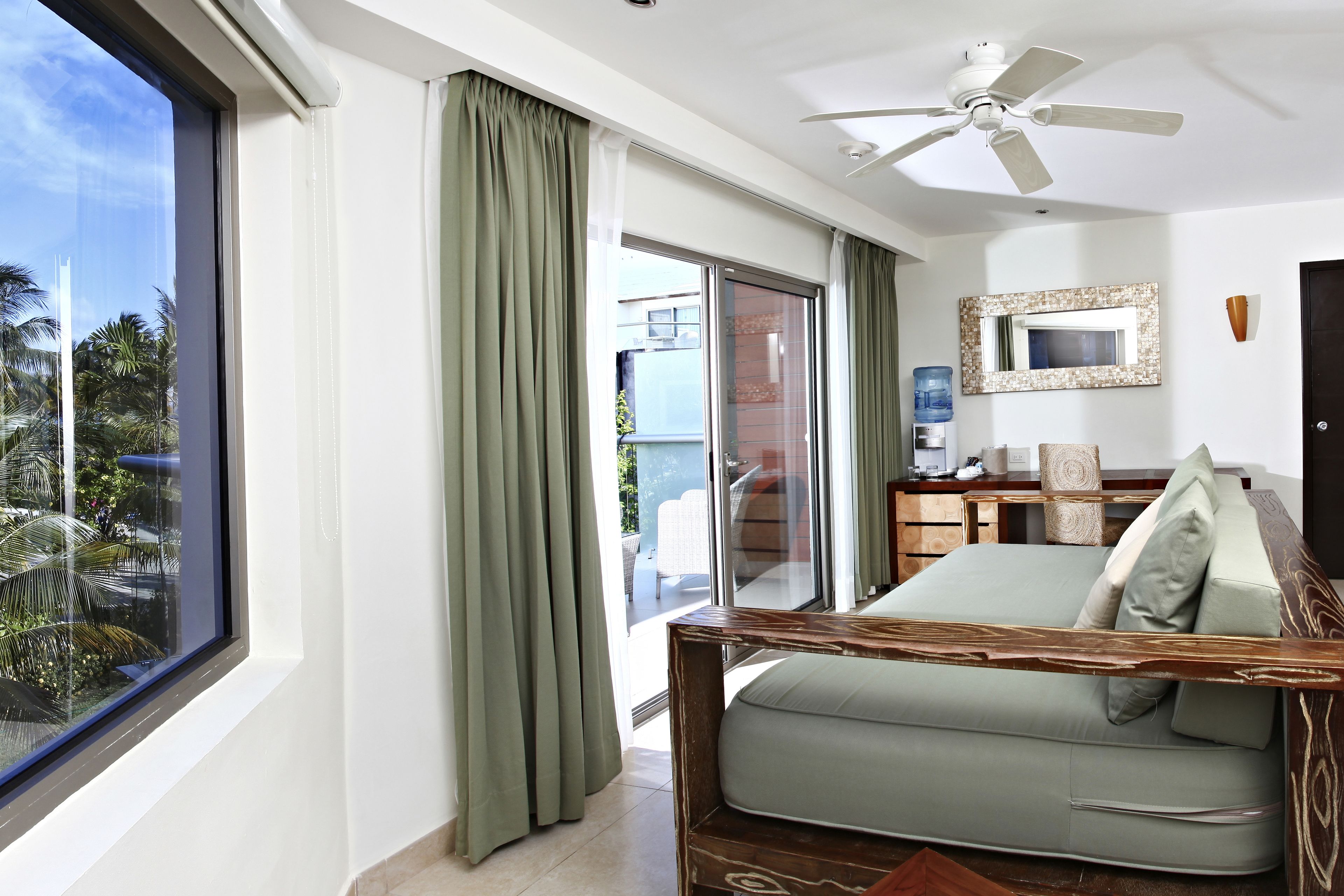 Ein modernes Zimmer mit großem Fenster, Deckenventilator, Sofa und Blick auf Palmen.
