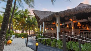 A resort walkway with thatched-roof structures, palm trees, and a sandy path. - Sandos Caracol Nature Resort & Water Park All Inclusive (Playa del Carmen)