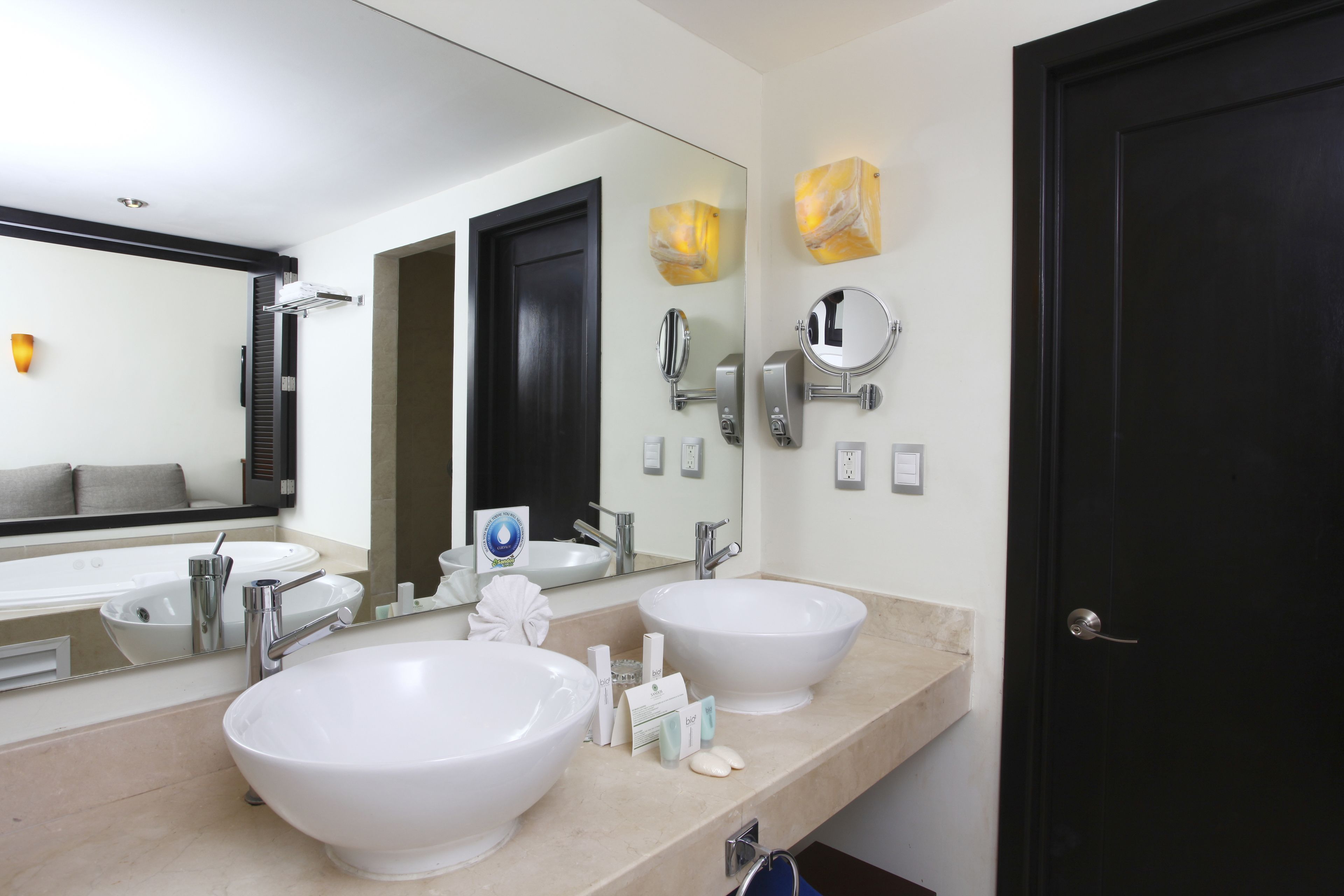 Un baño moderno con dos lavamanos grandes blancos, una puerta negra y un espejo con decoración de pared estilo mármol.