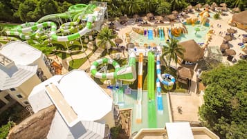 A water park with multiple slides and pools, surrounded by palm trees and thatched-roof huts.