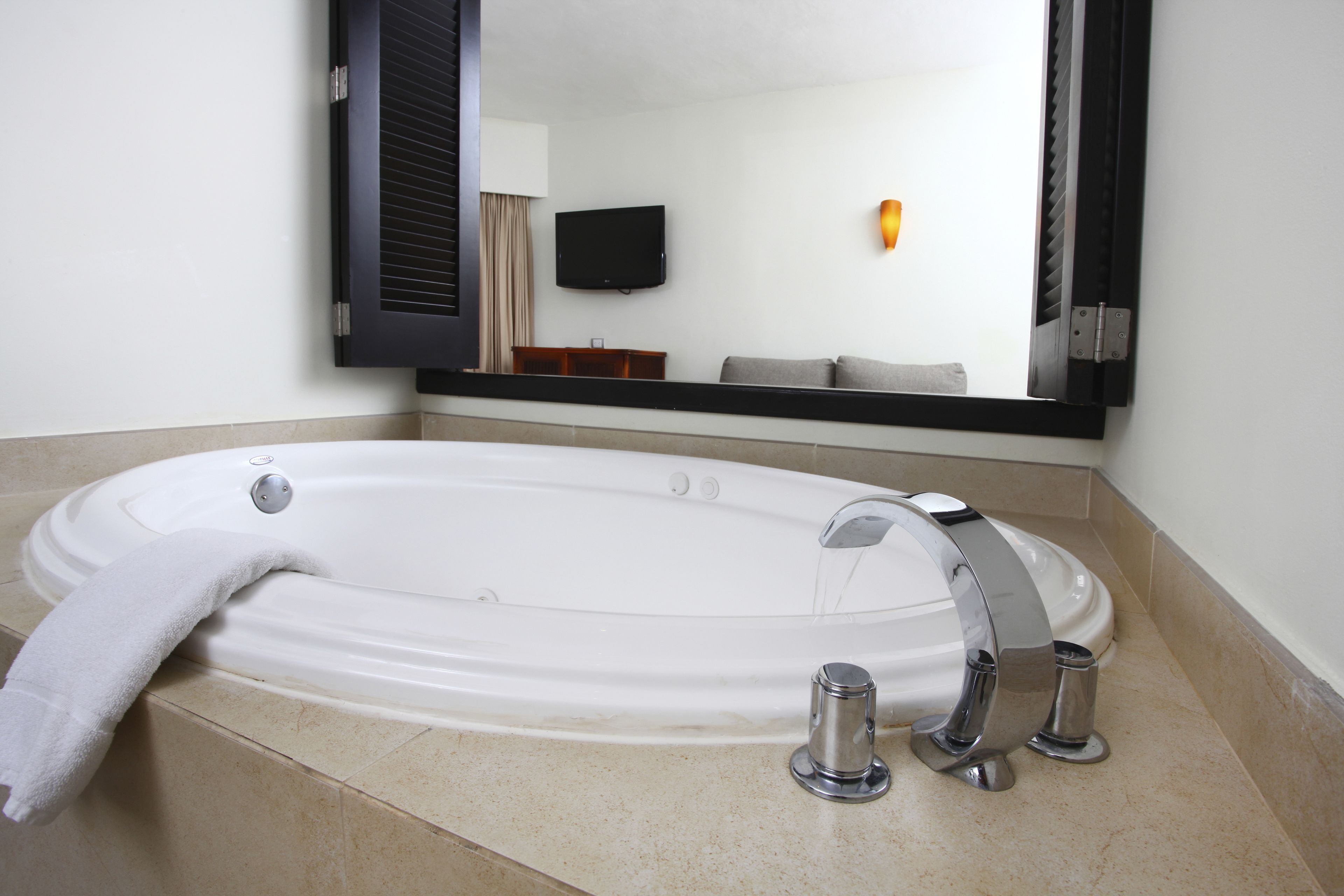 Un baño moderno con una bañera grande, un espejo y un televisor de pantalla plana montado en la pared.