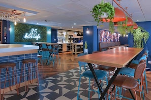 A bar/lounge area with a neon sign, bar stools, tables, and hanging plants. - Travelodge Leeds Vicar Lane (Leeds)