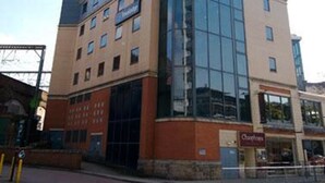 A multi-story hotel with a curved glass facade, a ground-level restaurant, and a parking lot. - Travelodge Leeds Vicar Lane (Leeds)