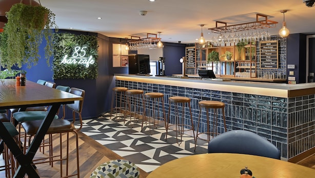 A bar area with a counter, stools, and a menu board listing drinks. - Travelodge Leeds Vicar Lane (Leeds)