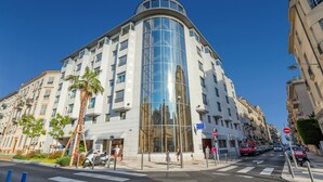 Un hotel moderno con fachada de vidrio curva, varios balcones y un paseo peatonal.